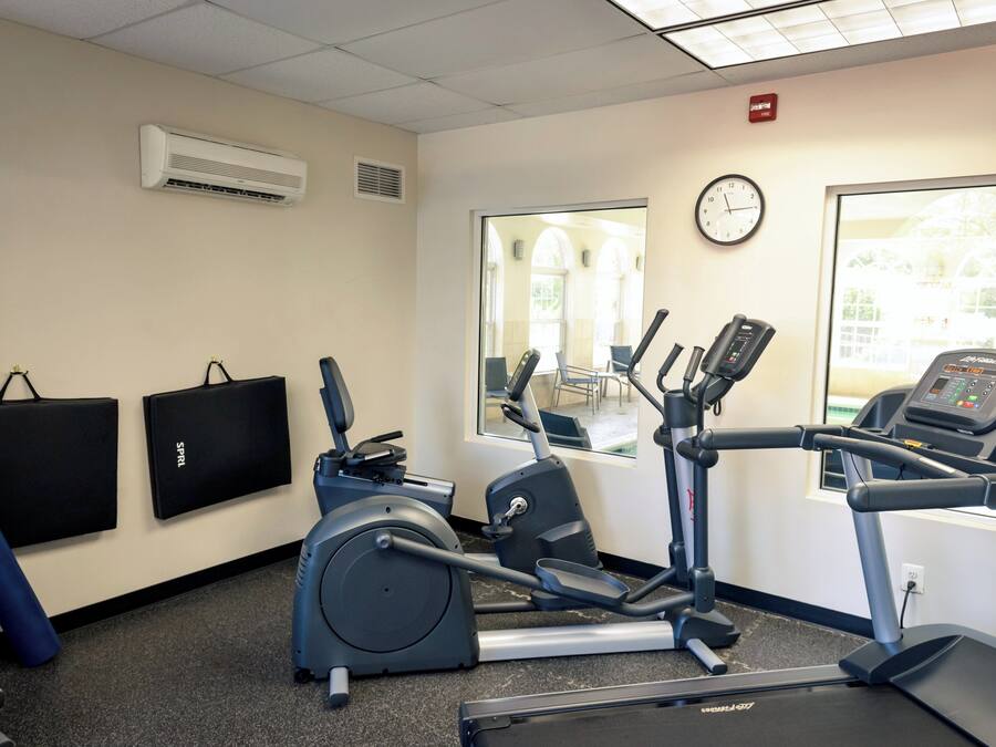 A fitness room with exercise equipment, a wall clock, and a window with a view of a building.