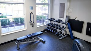 A gym with a bench, dumbbells, a yoga mat, and a wall-mounted TV.