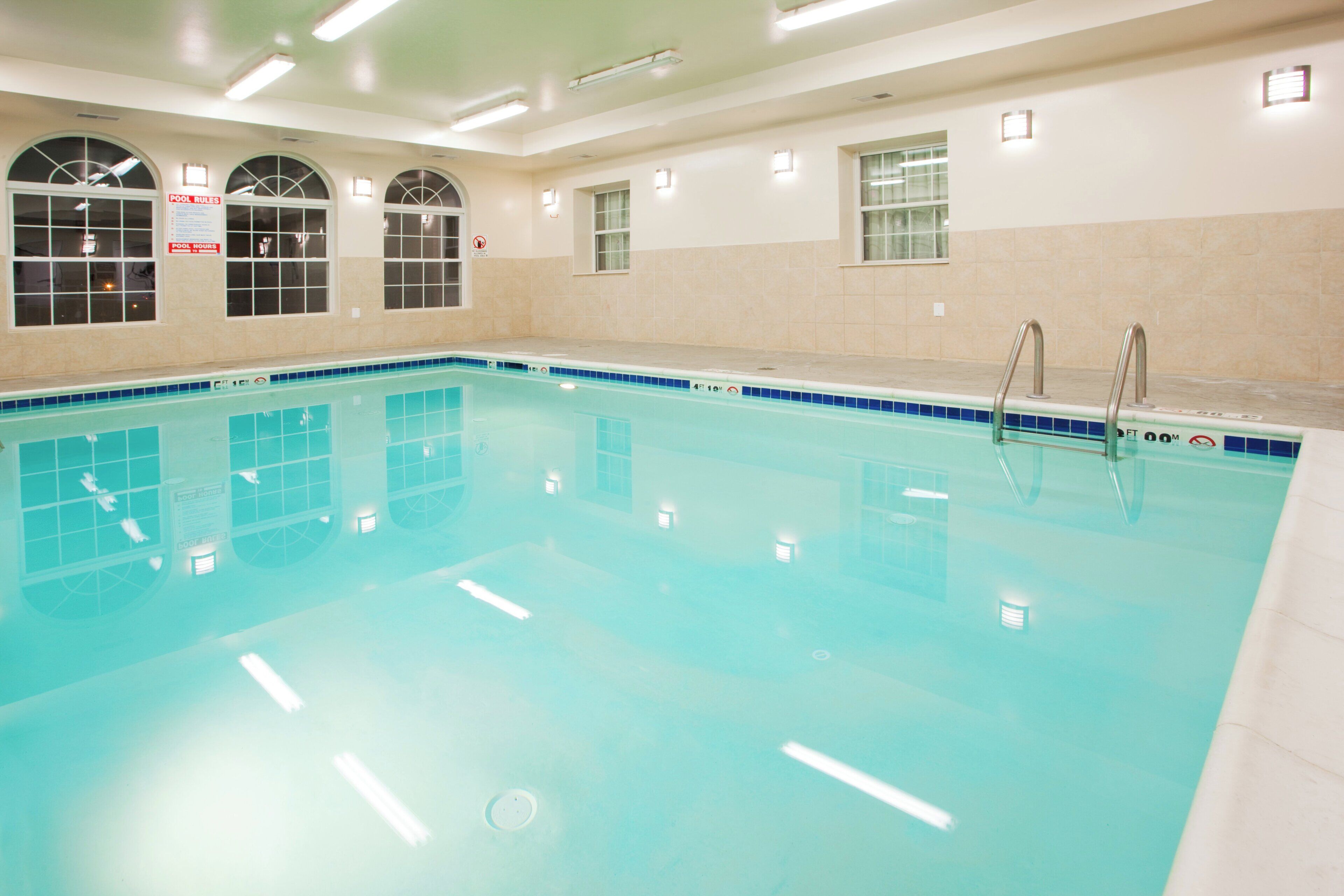 Una amplia piscina interior con agua cristalina, rodeada de paredes con ventanas y suelo de baldosas.