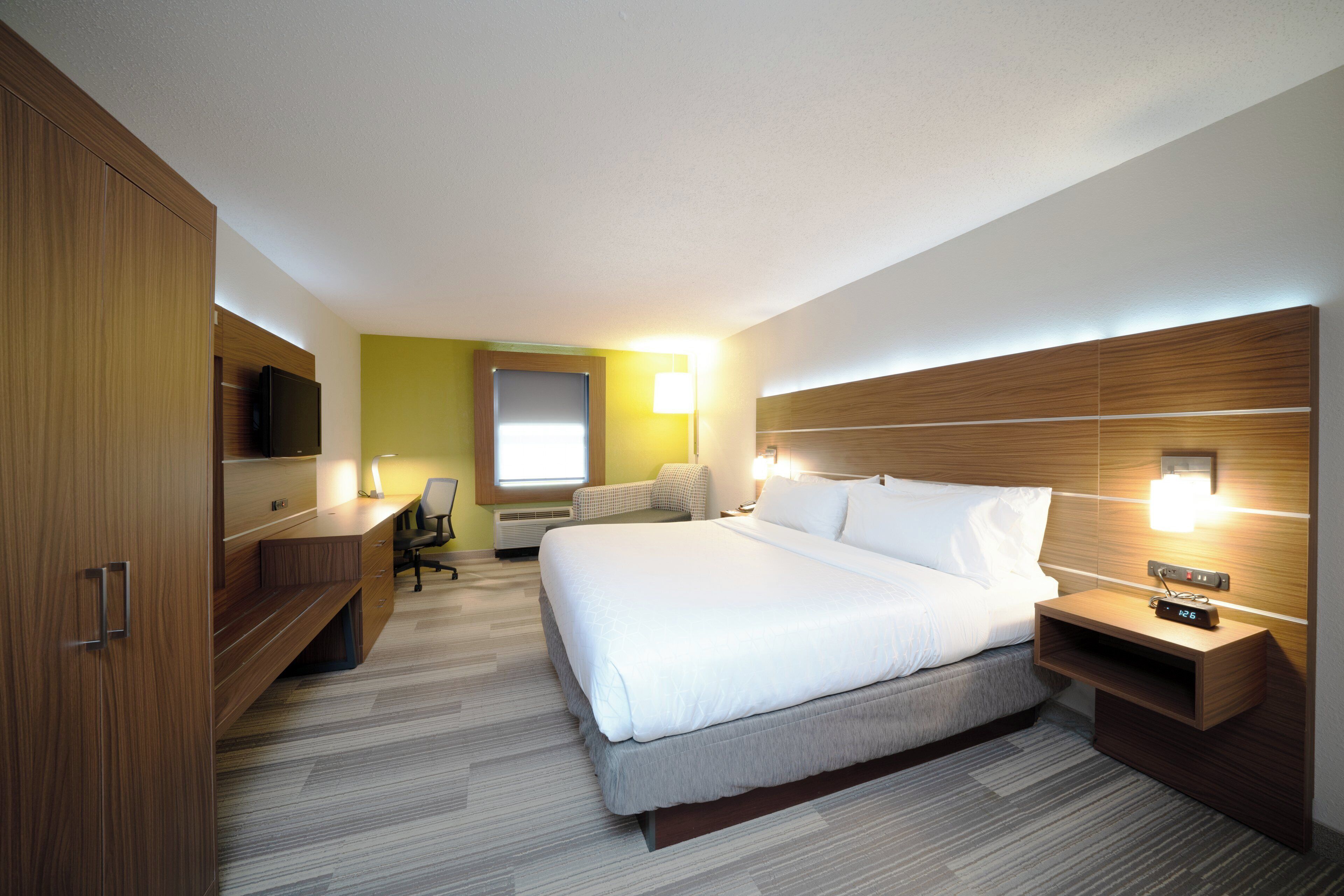 Una habitación de hotel con cama, mesita de noche, lámpara, escritorio, silla y televisor.