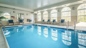 A swimming pool with clear blue water, surrounded by sunlit arched windows and a row of chairs.