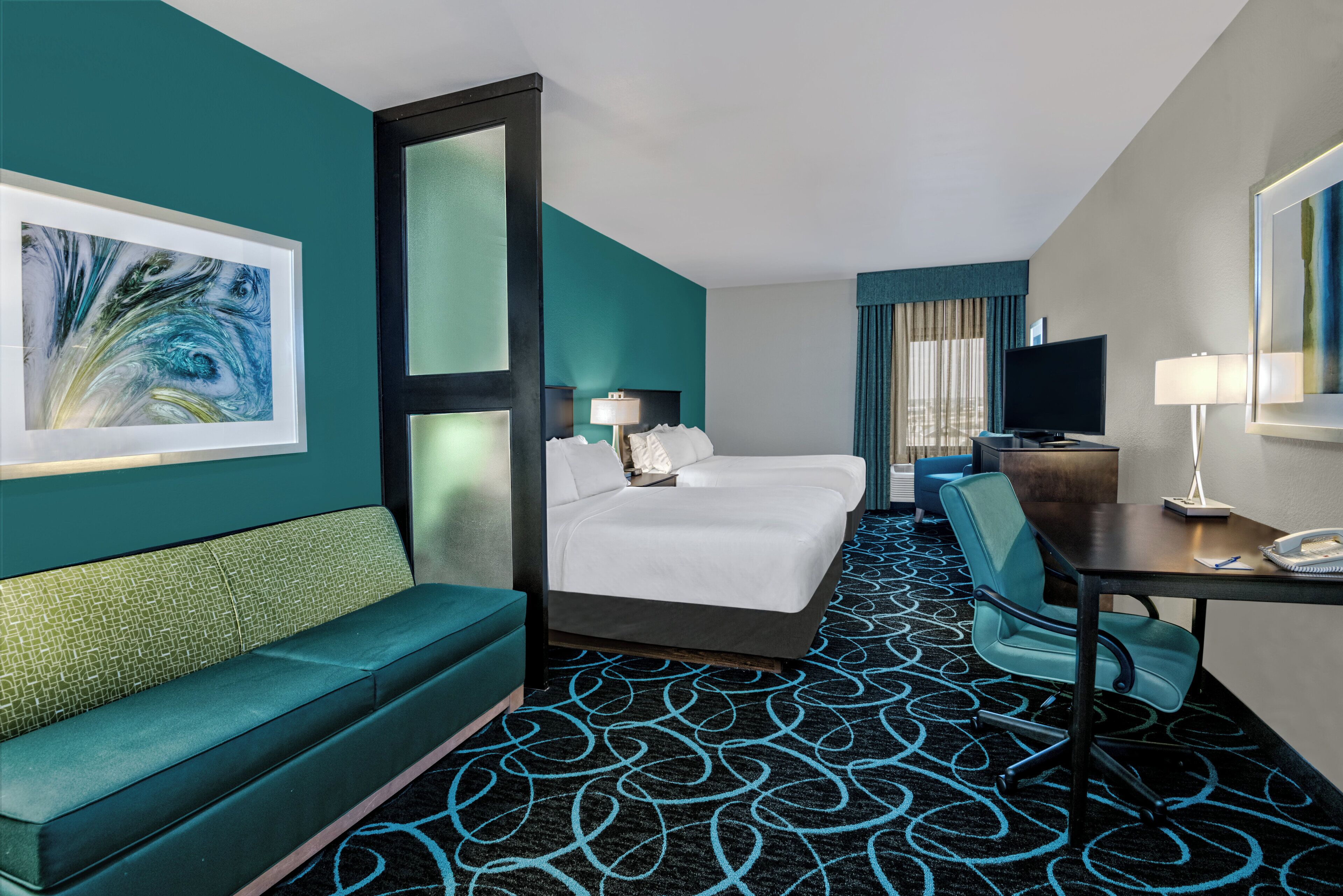 Une chambre d’hôtel avec un lit, un bureau, une chaise, un canapé et un grand tableau au mur.