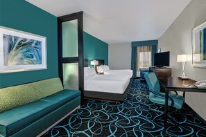 Une chambre d’hôtel avec un lit, un bureau, une chaise, un canapé et un grand tableau au mur.