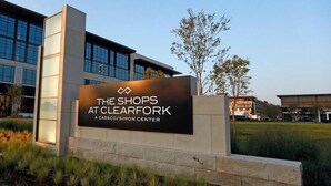 Placa de 'The Shops at Clearfork' com um edifício moderno ao fundo.