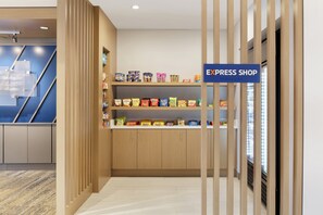 A hotel lobby with a wooden reception desk, a blue sign reading "EXPRESS SHOP," and shelves stocked with snacks. - Holiday Inn Express Hotel & Suites Fort Worth Southwest I-20 by IHG (Fort Worth)