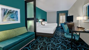 Quarto de hotel com cama, sofá, escrivaninha e televisão.