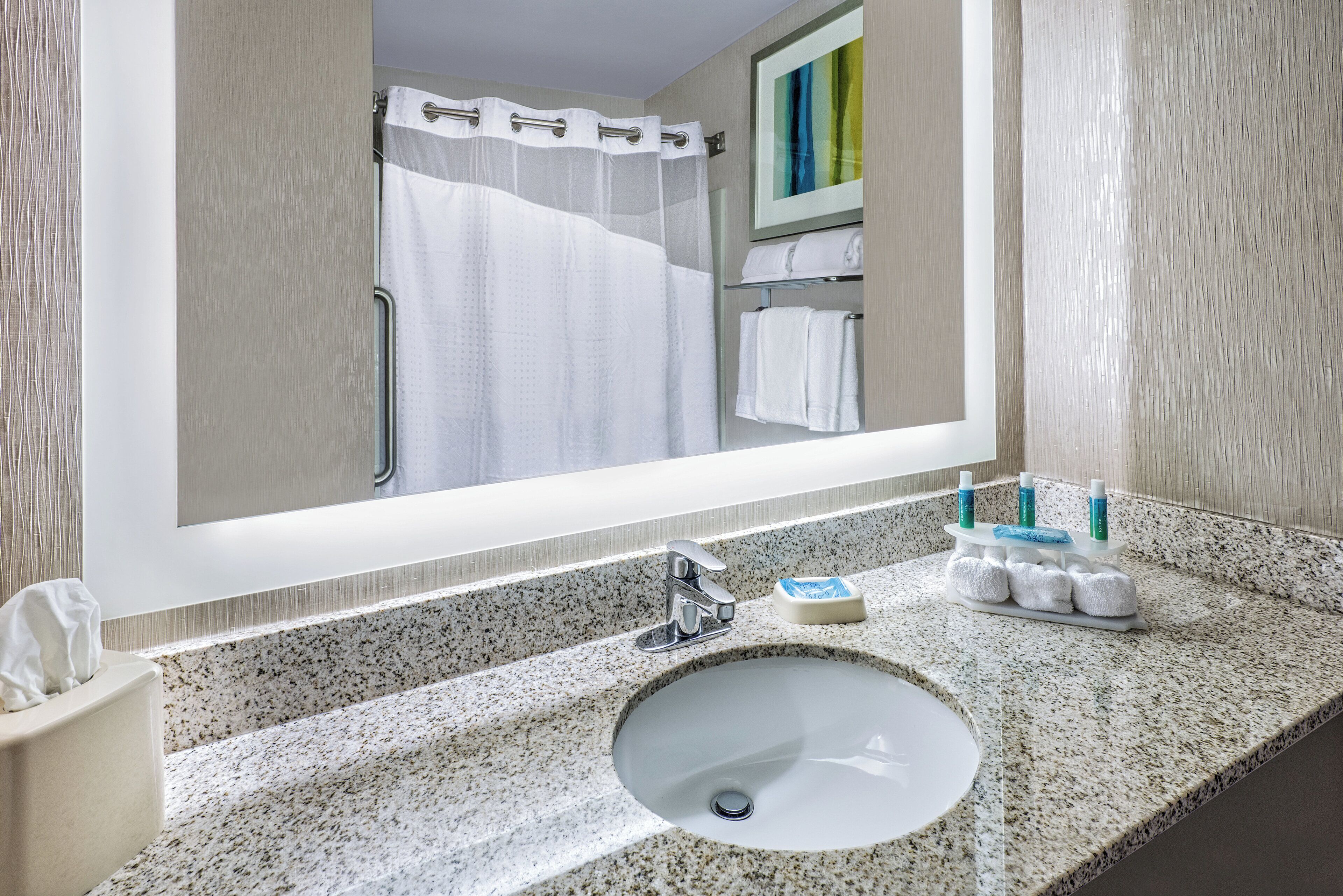 A bathroom with a granite countertop, a white sink, a mirror, a shower curtain, and a towel rack with towels.