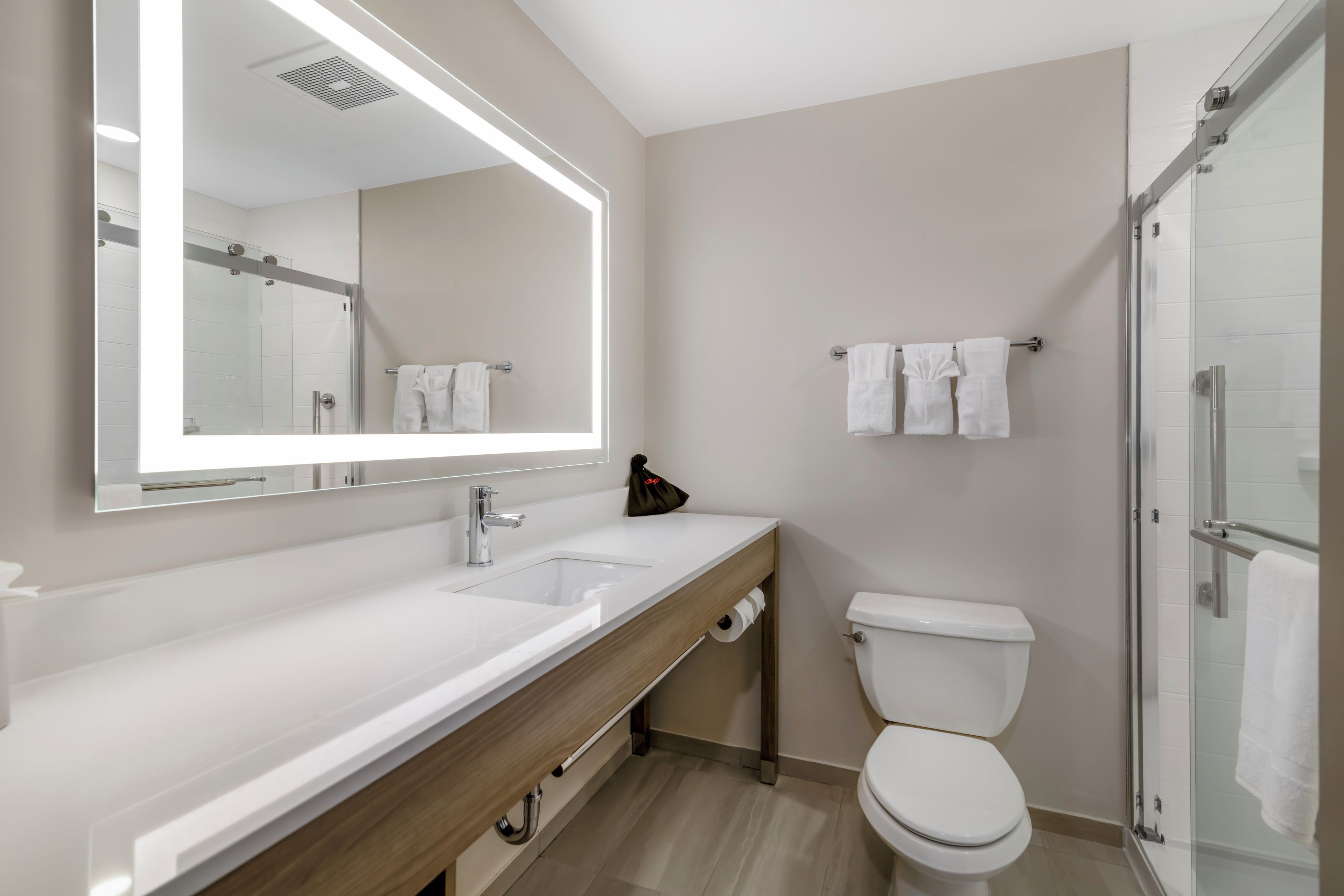 A modern bathroom with a large mirror, a sink, a toilet, and a shower area.