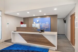 Una recepción de hotel con diseño moderno, alfombra azul y detector de incendios en la pared.