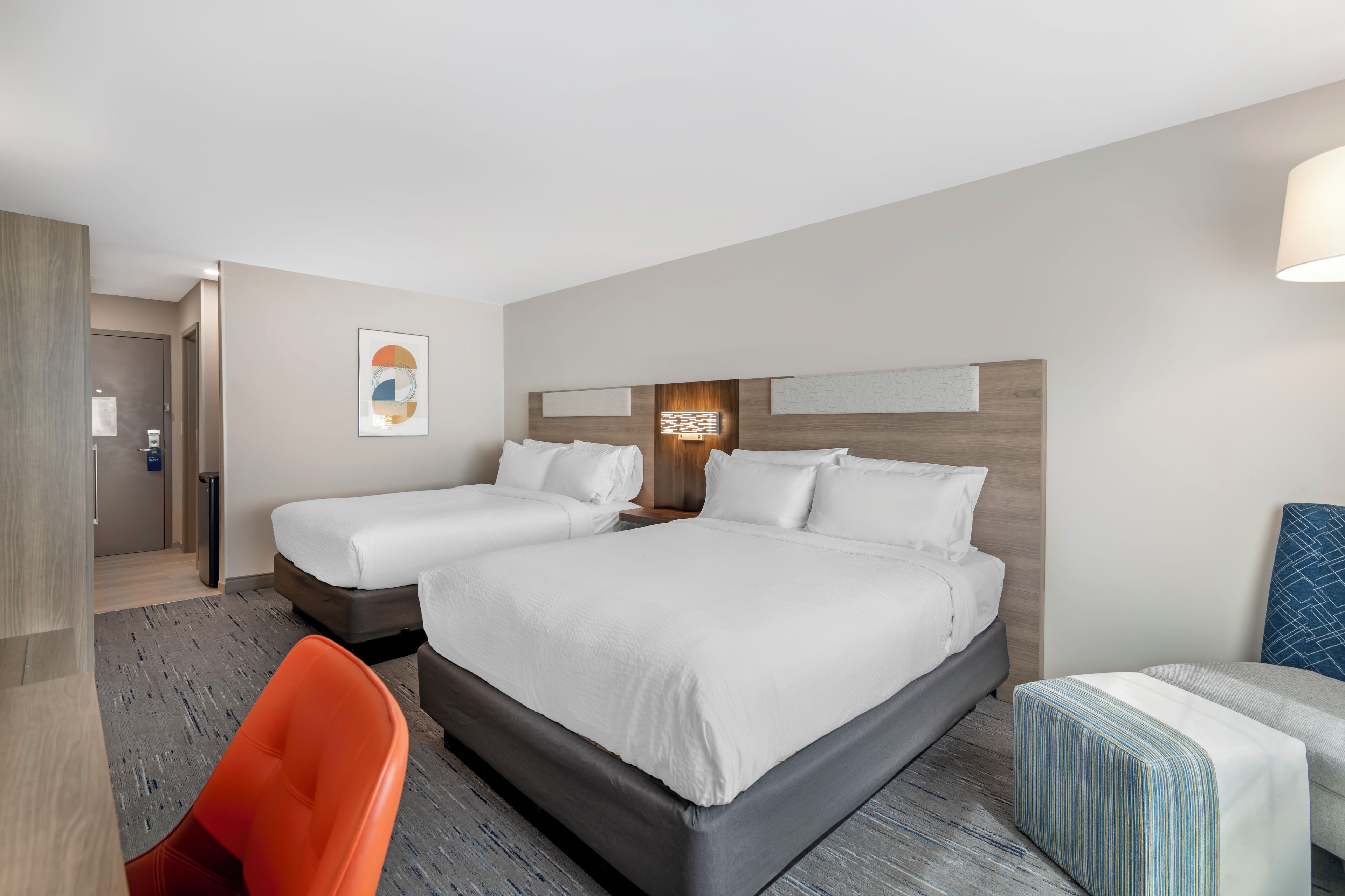A hotel room with a large bed, a smaller bed, a desk, and a chair.