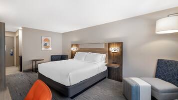 A hotel room with a large bed, a desk, a chair, and a small table.