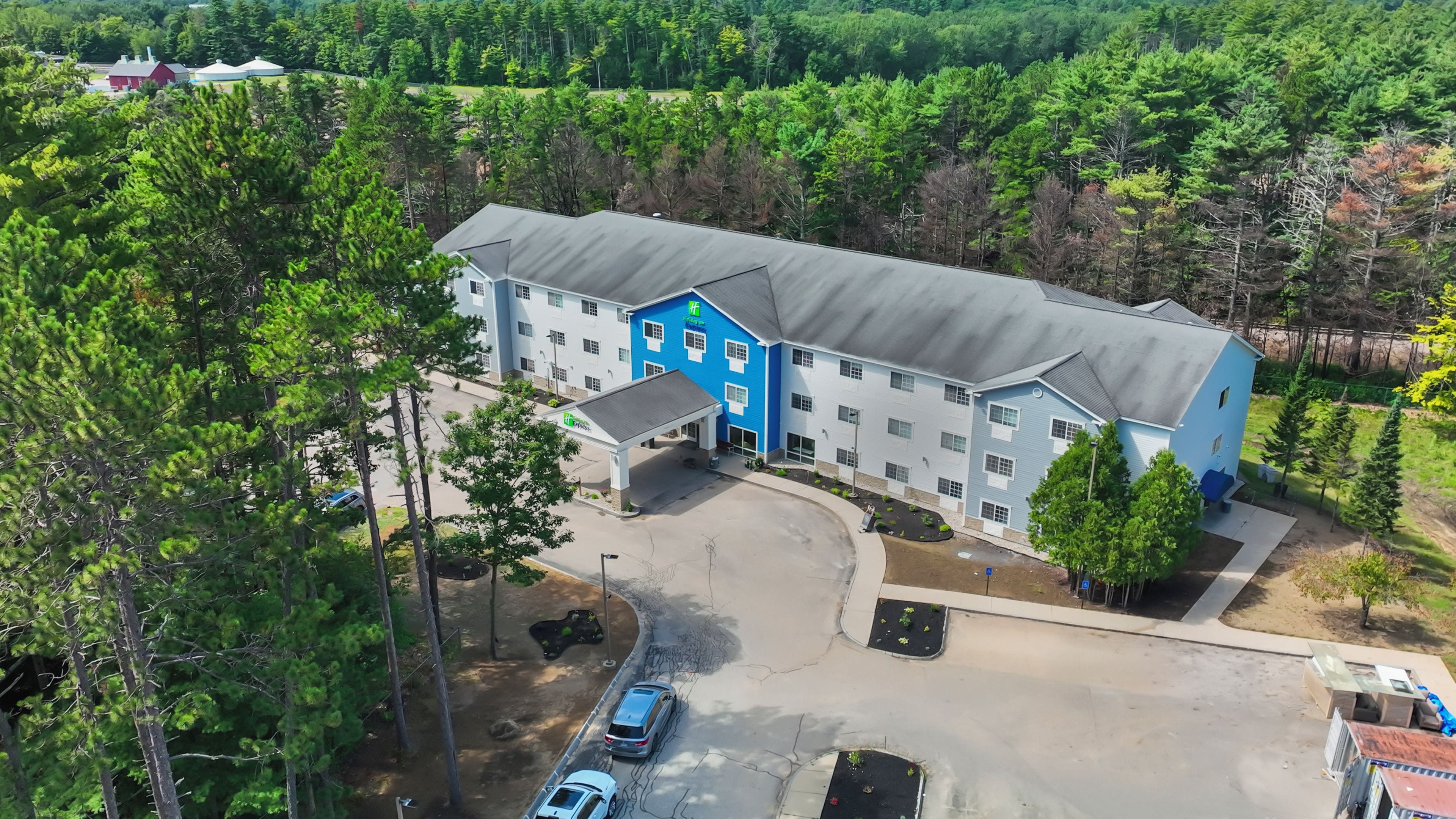 A multi-story hotel with a blue and white facade, a parking lot, and a surrounding forested area.