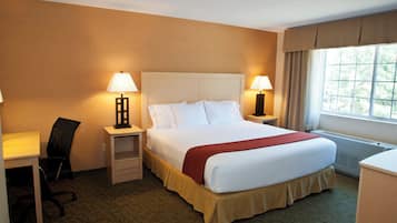 A hotel room with a bed, two bedside tables with lamps, a chair, a desk, and a window with curtains.