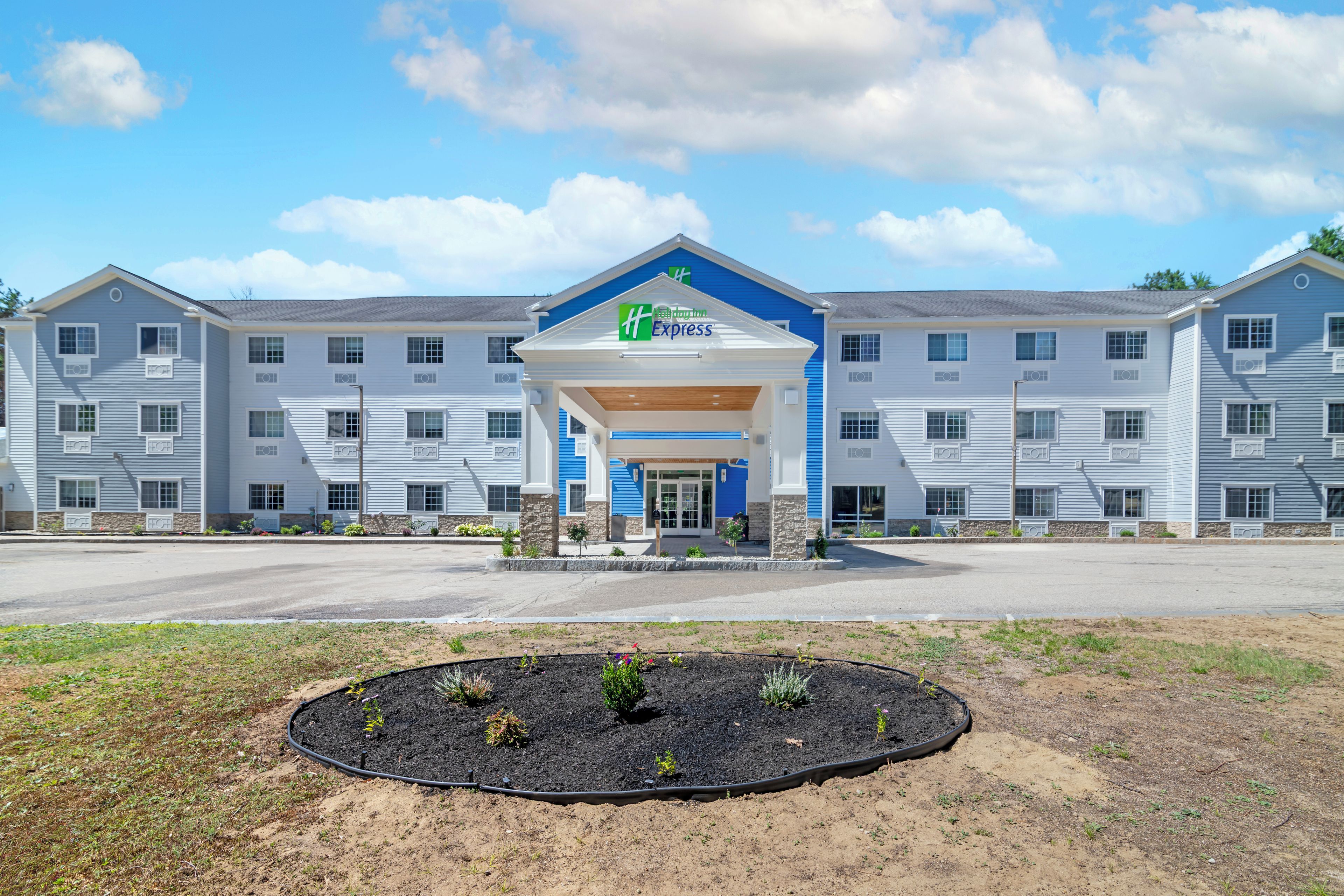 Hotel com entrada central, várias janelas e área ajardinada com plantas.