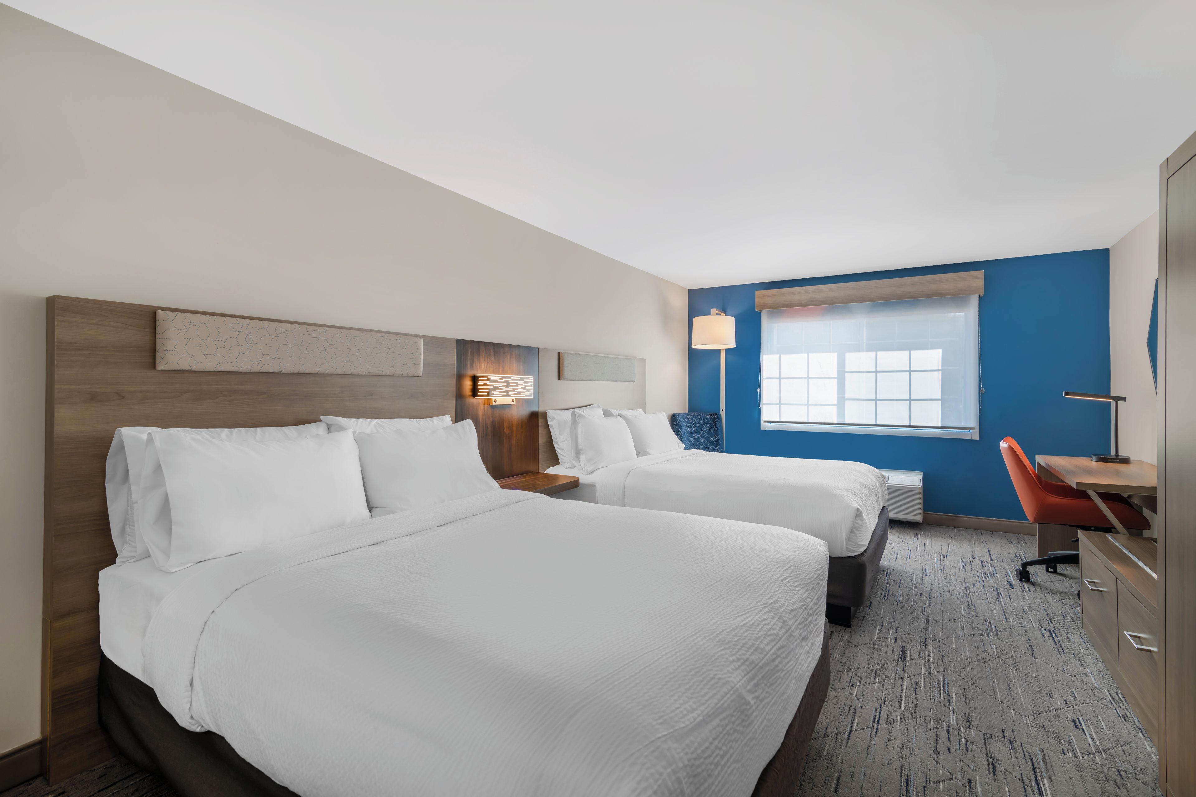 Quarto de hotel com duas camas, uma escrivaninha e uma cadeira.