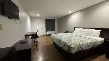 A hotel room with a bed, a desk, a chair, a TV mounted on the wall, and a door.