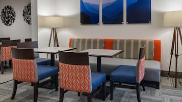 A hotel room with a dining area featuring tables and chairs, a sofa, and two wall-mounted lamps.