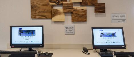 Two computer desks with monitors, a business center sign, and a wall with wooden panels.