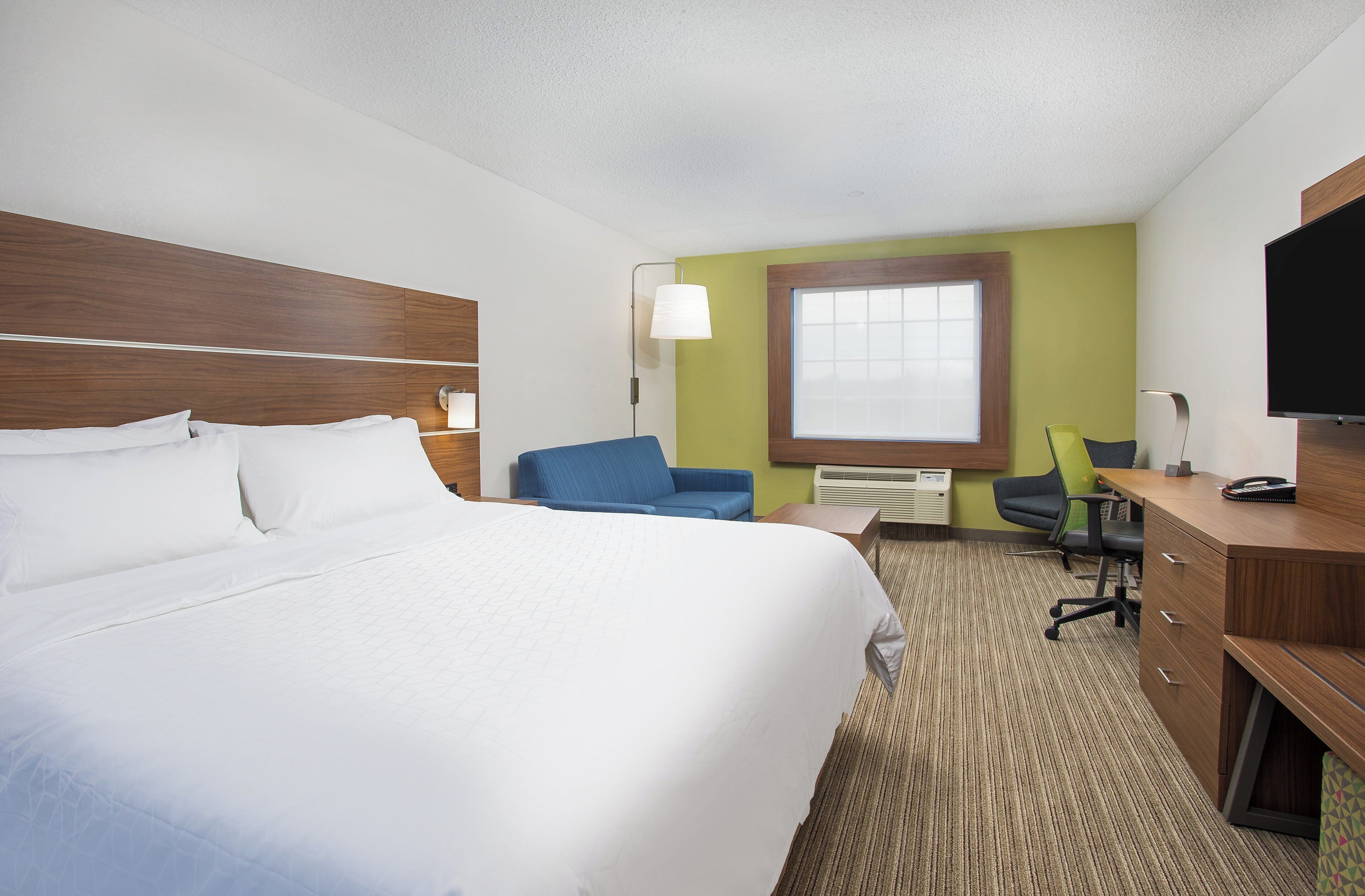 A hotel room with a large bed, a desk, a chair, a television, and a window.