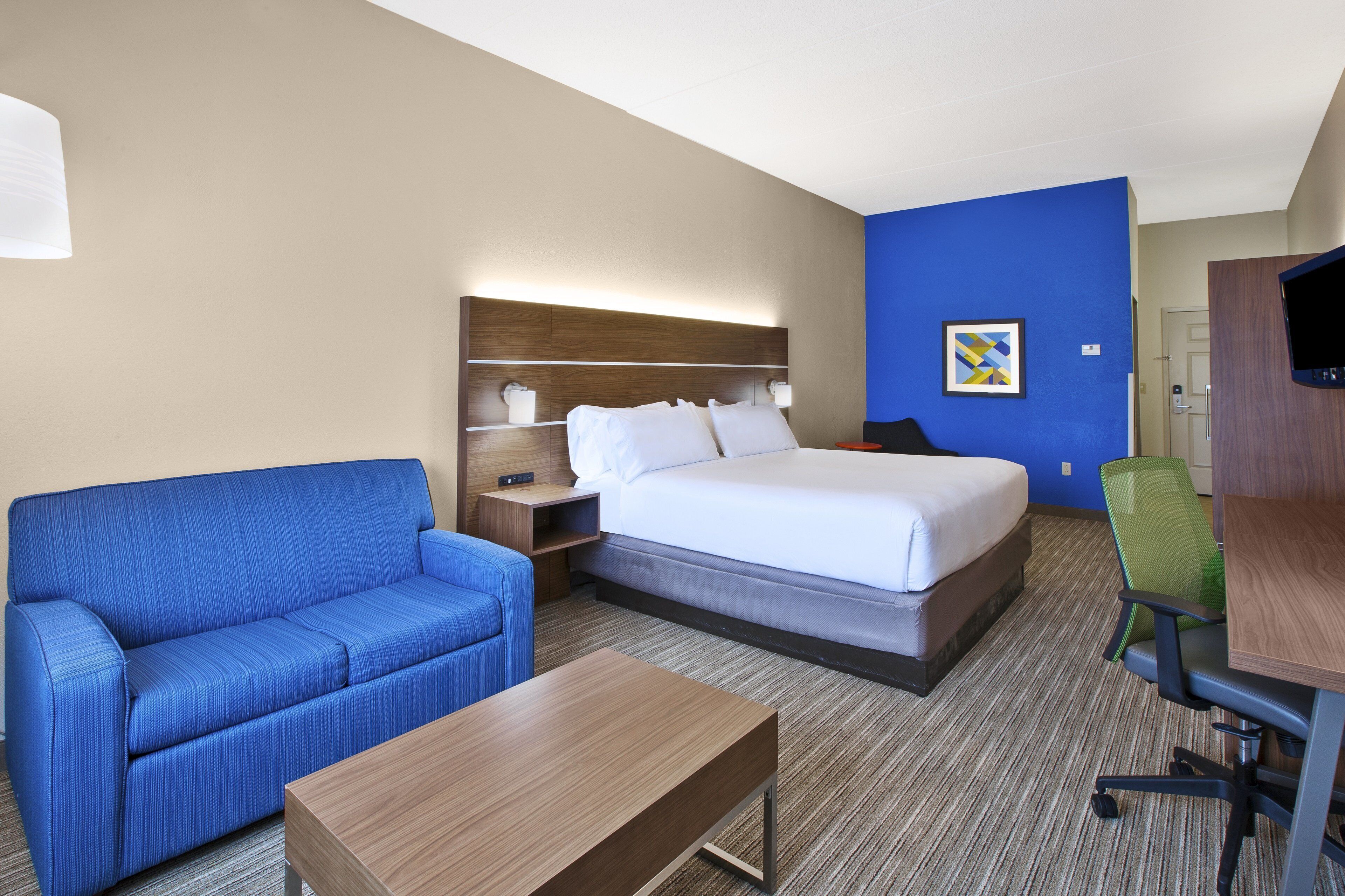 Une chambre d’hôtel avec un lit, un canapé bleu, une table basse en bois, un bureau avec une chaise et un téléviseur.