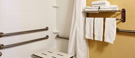 A bathroom with white tiles, a shower with a white curtain, and a towel rack with folded towels.