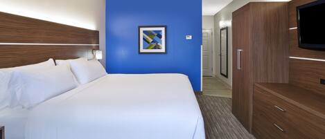 A hotel room with a large bed, a TV, wooden furniture, and a blue accent wall.
