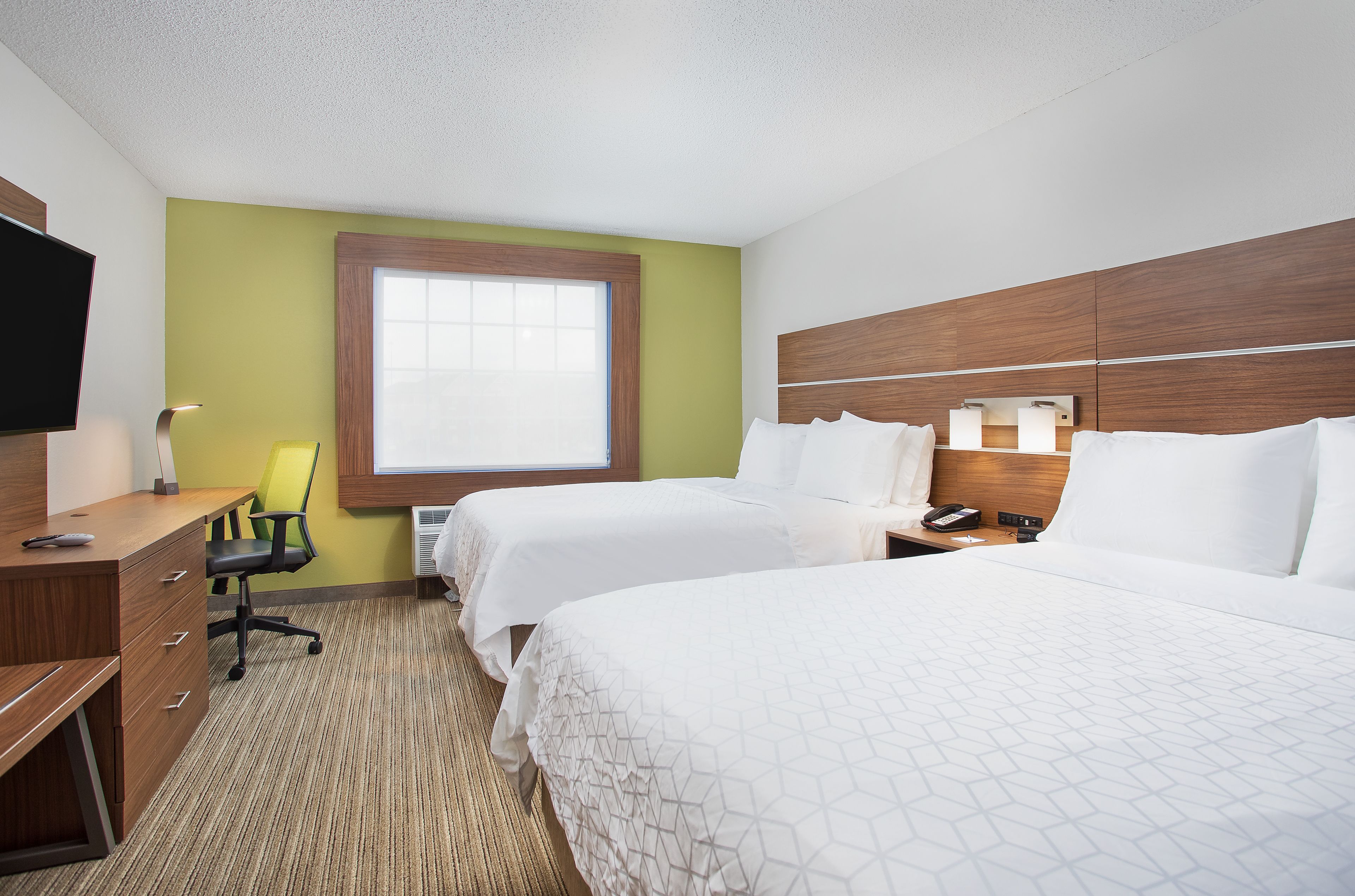 A hotel room with two beds, a desk, a chair, a TV, and a window.