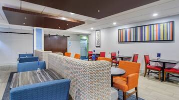 Un hall d’hôtel avec un long comptoir, des sièges bleus et orange, et une peinture abstraite colorée accrochée au mur.