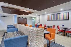A hotel lobby with a long counter, blue and orange seating, and a colorful abstract painting on the wall. - Holiday Inn Express & Suites Alcoa (Knoxville Airport) by IHG (Alcoa)