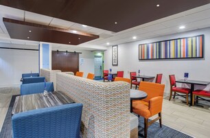 Un vestíbulo de hotel con una larga recepción, asientos azul y naranja, y un cuadro abstracto colorido en la pared.