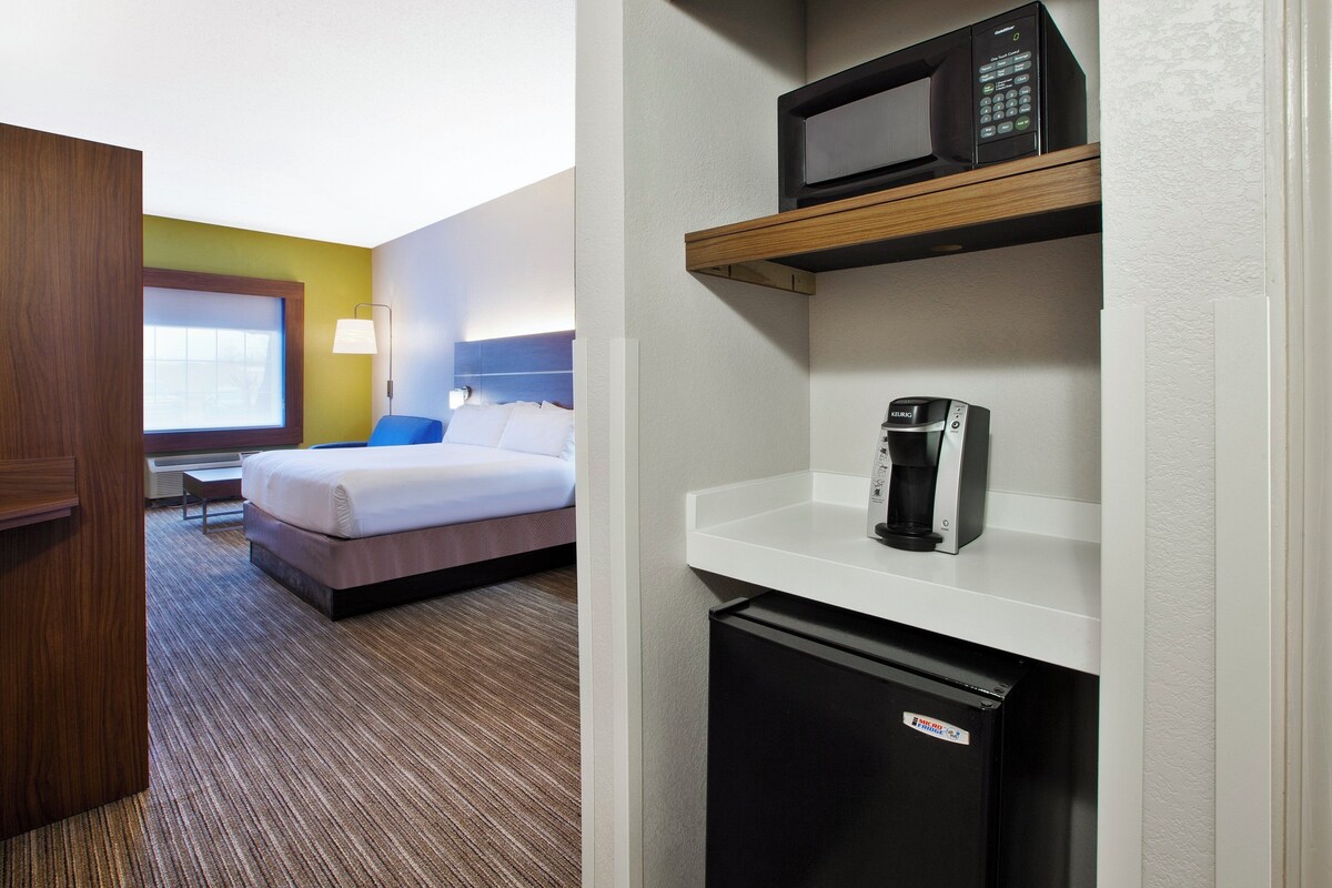 A hotel room with a bed, a microwave, a coffee maker, and a refrigerator.