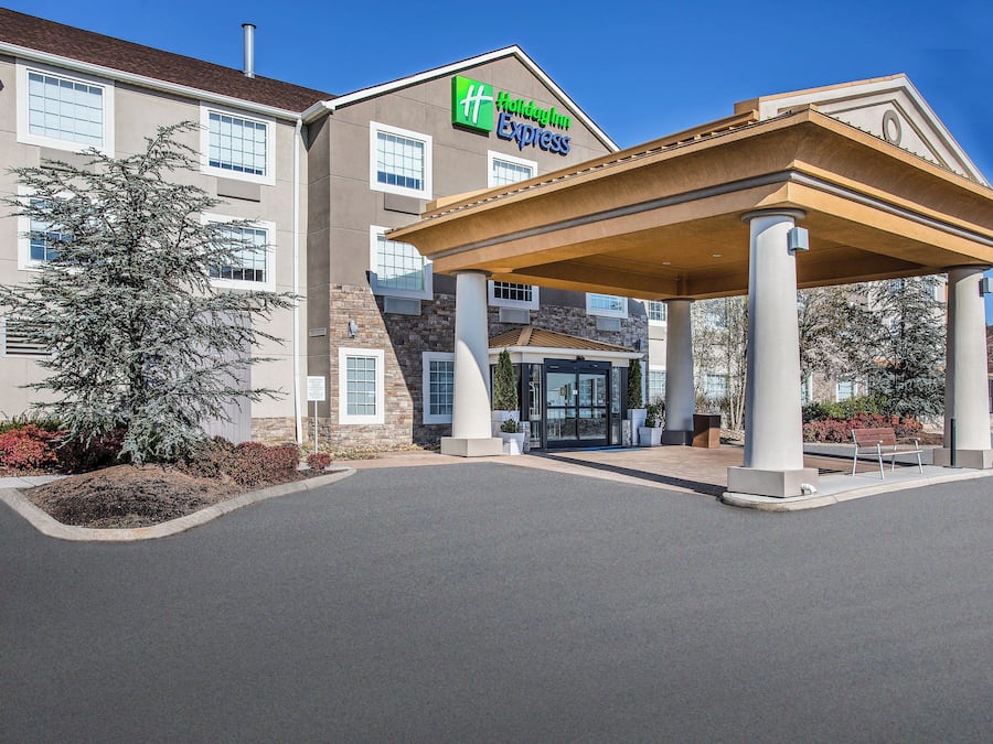 Edifício Holiday Inn Express com entrada coberta e área ajardinada com arbustos e uma árvore.