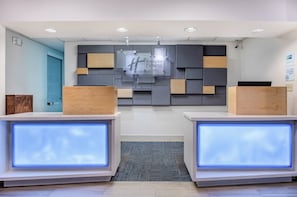 Un comptoir d’accueil d’hôtel au design moderne, avec une enseigne Holiday Inn Express, un panneau indiquant qu’il est interdit de fumer et une caméra de surveillance.