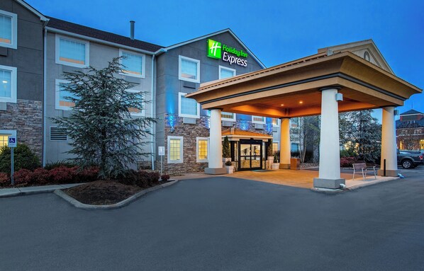 Un hotel Holiday Inn Express con entrada cubierta, fachada de piedra y estacionamiento.