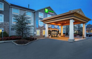 Un hotel Holiday Inn Express con entrada cubierta, fachada de piedra y estacionamiento.