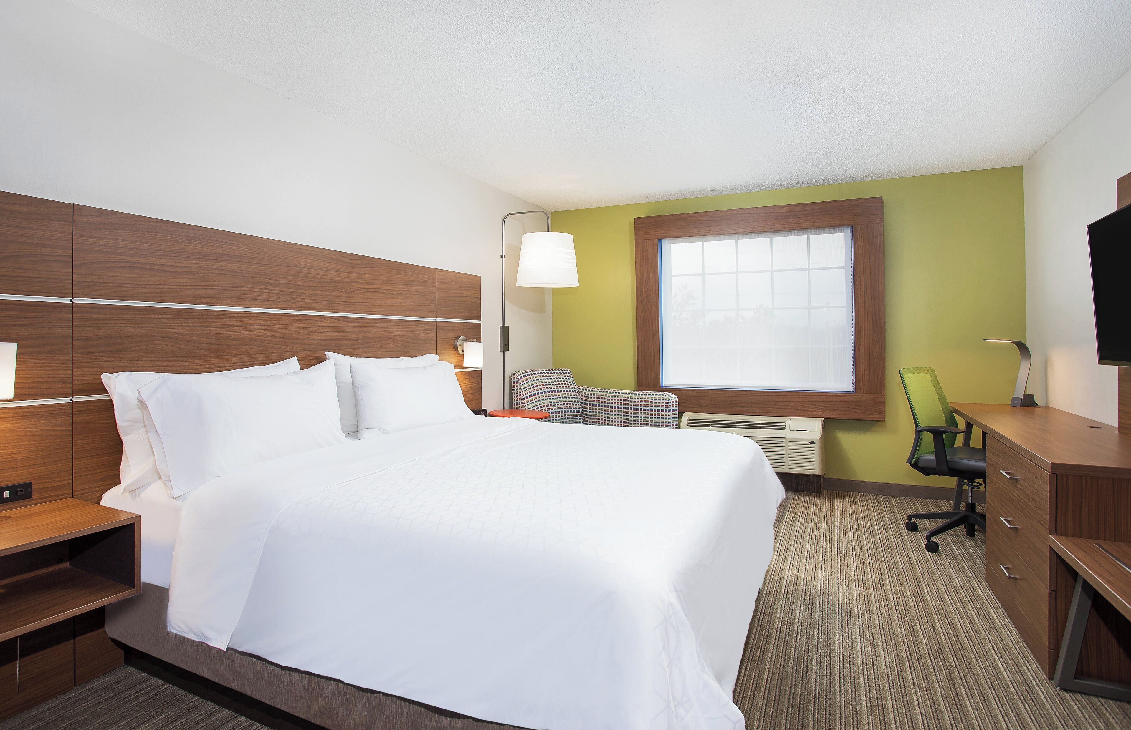 A hotel room with a bed, bedside table, lamp, chair, desk, and TV.