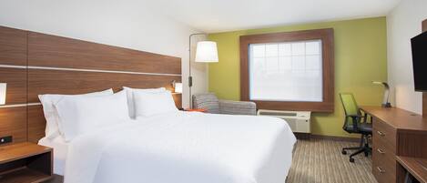 A hotel room with a bed, bedside table, lamp, chair, desk, and TV.