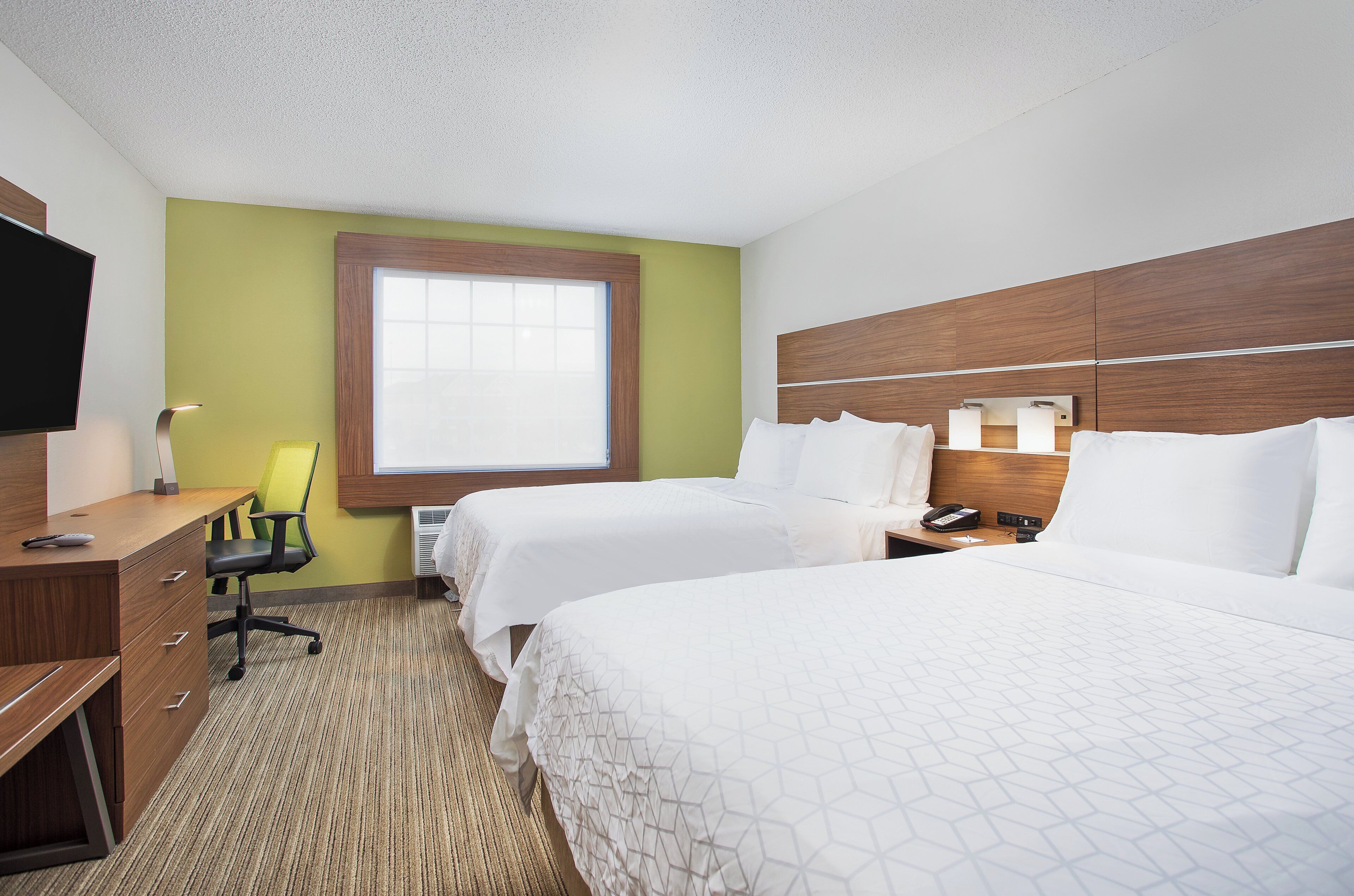A hotel room with two beds, a desk, a chair, a television, and a window.