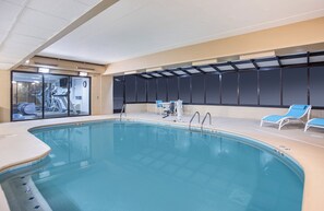Ein Hallenbad mit klarem Wasser, einigen Liegestühlen und einer Glastür zu einem Fitnessbereich mit Laufbändern.