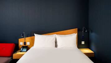 A hotel room with a bed, bedside tables, a red chair, a phone, and a lamp.