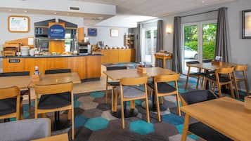 Un espace pour le petit-déjeuner à l’hôtel, avec un buffet, des tables et des chaises, et une vue sur l’extérieur.