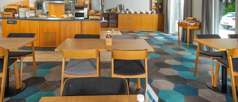 A breakfast area with tables, chairs, and a counter with breakfast items.