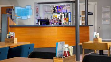 Zona de bar con mostrador, taburetes y una variedad de botellas y vasos.