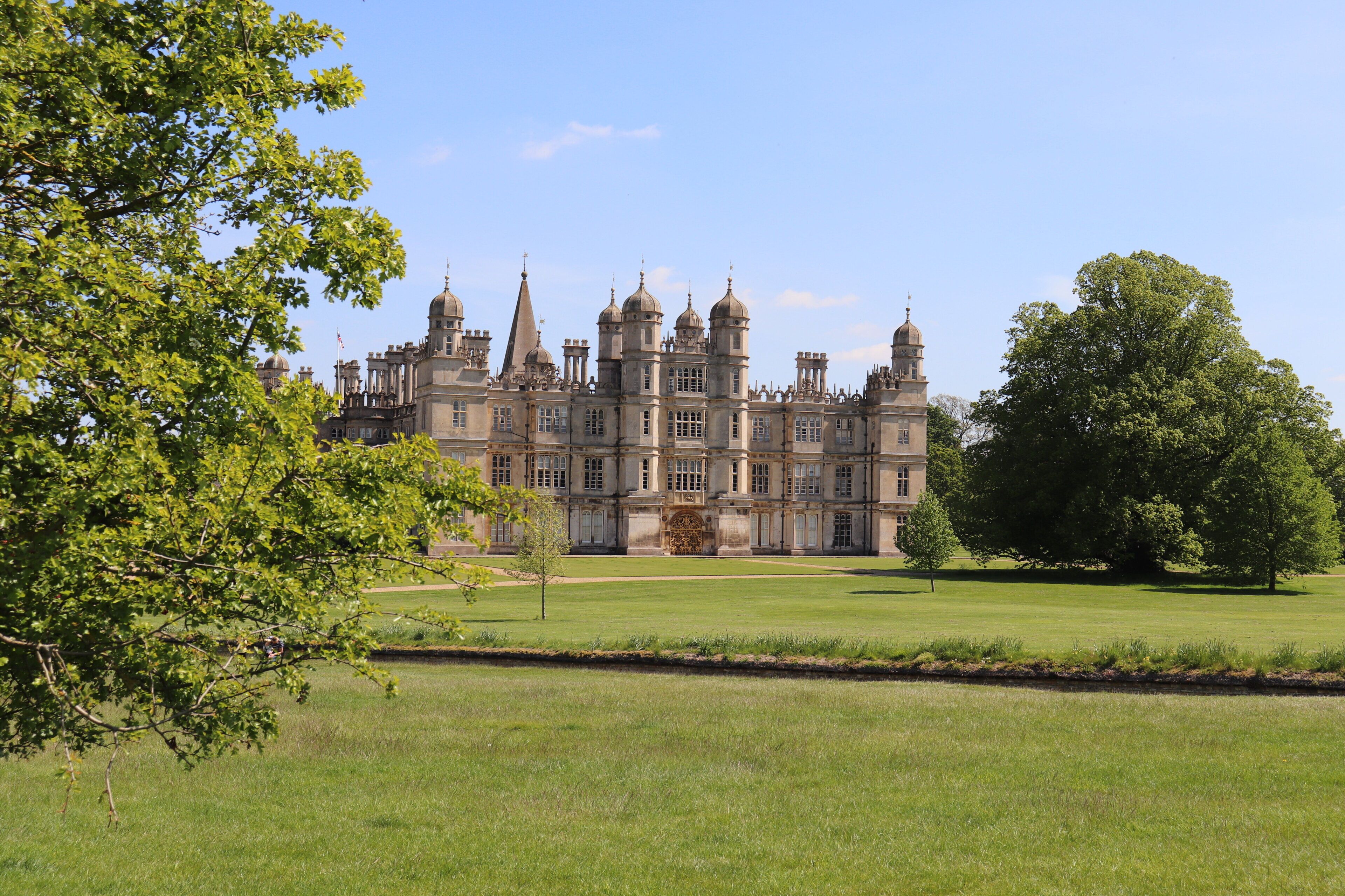 A large, historic building with multiple towers and a symmetrical facade, surrounded by a well-maintained lawn and trees.