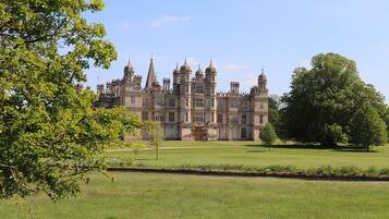 A large, historic building with multiple towers and a symmetrical facade, surrounded by a well-maintained lawn and trees.