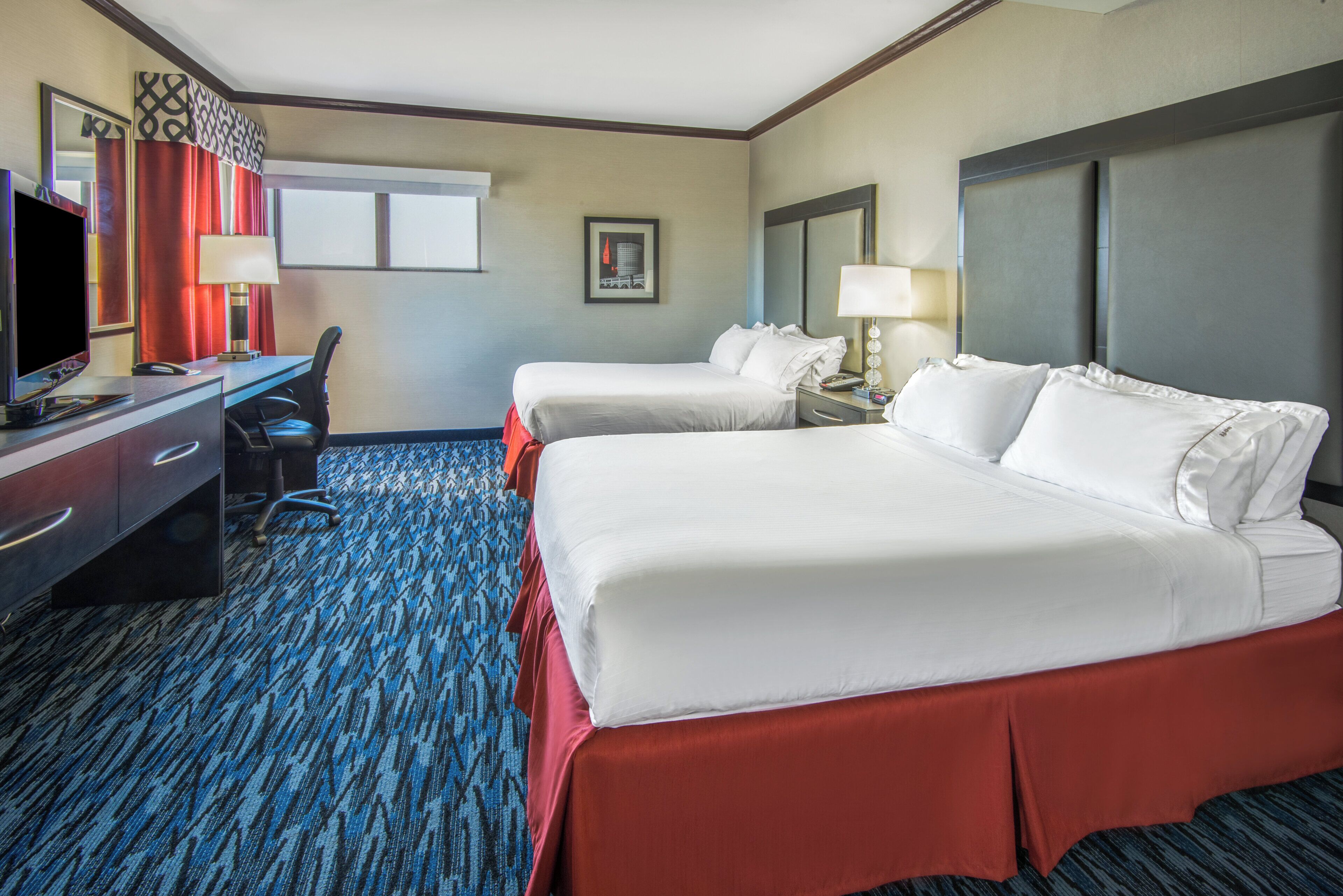 A hotel room with two beds, a desk with a computer, a TV, and a window with curtains.