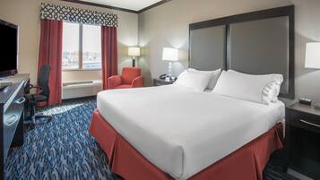 Habitación de hotel con una cama grande, un escritorio con silla, televisión y ventana con cortinas.