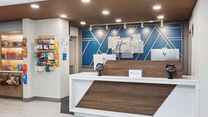 A hotel reception desk with a modern design, featuring a wooden counter and a blue geometric wall. - Holiday Inn Express Cleveland Airport - Brookpark by IHG (Brook Park)