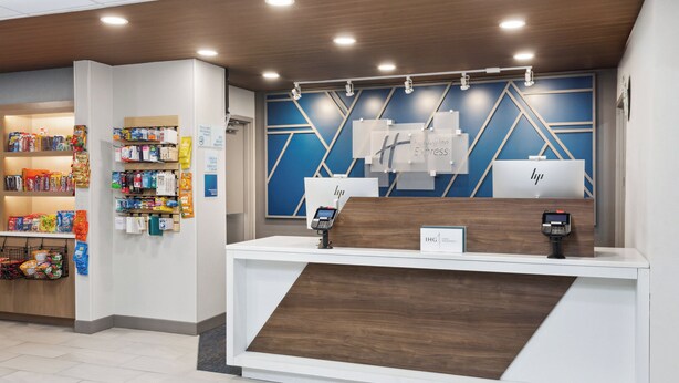 A hotel reception desk with a modern design, featuring a wooden counter and a blue geometric wall. - Holiday Inn Express Cleveland Airport - Brookpark by IHG (Brook Park)