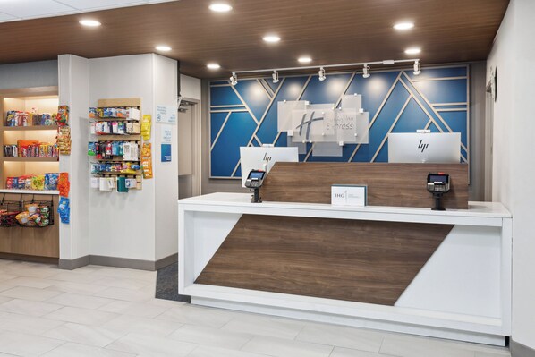 A hotel reception desk with a modern design, featuring a wooden counter and a blue geometric wall. - Holiday Inn Express Cleveland Airport - Brookpark by IHG (Brook Park)